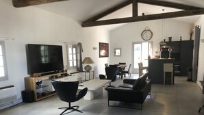 A spacious living area with a large TV, comfortable seating, a dining table, and a kitchen in the background.