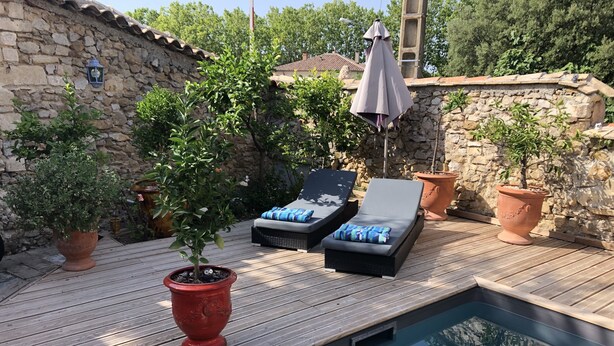 A wooden deck with a swimming pool, lounge chairs, and potted plants.