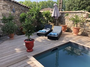 A wooden deck with a swimming pool, lounge chairs, and potted plants.