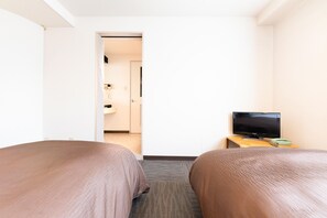 Habitación de hotel con dos camas, un televisor sobre una mesita auxiliar y un baño visible a través de una puerta abierta.