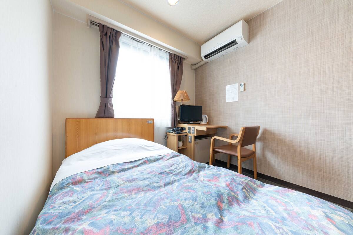 Una habitación de hotel con una cama, un escritorio con computadora, una silla y un equipo de aire acondicionado.