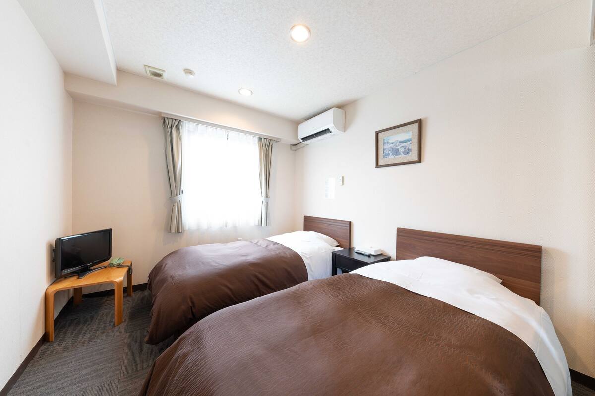 Habitación de hotel con dos camas, un televisor sobre una mesita y una ventana con cortinas.