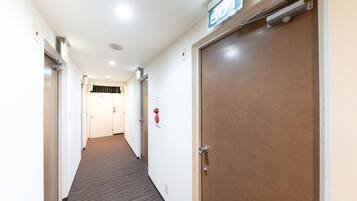 Un pasillo de hotel con piso alfombrado, una puerta con el número 501 y un detector de incendios en la pared.