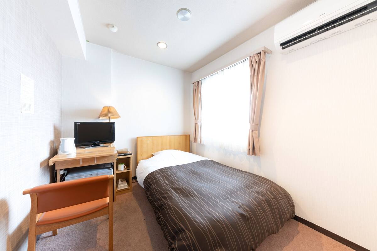 Habitación de hotel con una cama, un escritorio con computadora, una silla, una lámpara y un equipo de aire acondicionado.