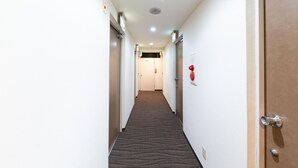 Un couloir d'hôtel avec des revêtements de sol en moquette, des murs blancs et des portes de part et d'autre.