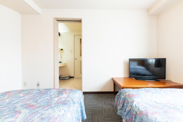 Une chambre d’hôtel avec deux lits, un téléviseur posé sur une table en bois et une salle de bain visible à travers une porte ouverte.