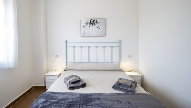Une chambre à coucher avec un lit, deux tables de chevet, un tableau accroché au mur et une fenêtre avec des rideaux.
