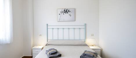 A bedroom with a bed, two bedside tables, a wall-mounted picture, and a window with curtains.