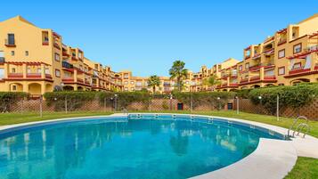Piscina rodeada por edifícios altos com varandas e um céu azul límpido.