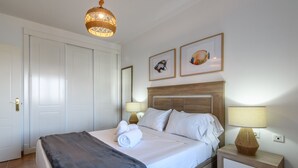 A neatly arranged hotel room with a bed, bedside lamps, a nightstand, and a door. - Marina III - Marina Isla Canela PMHIII37P5 (Punta del Moral)