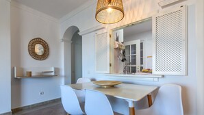 A dining area with a white table, four white chairs, a wooden floor, a hanging light fixture, and a wall-mounted mirror. - Marina III - Marina Isla Canela PMHIII37P5 (Punta del Moral)