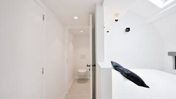 A modern bedroom with a skylight, a bed with a black pillow, and a white wall with a light switch.