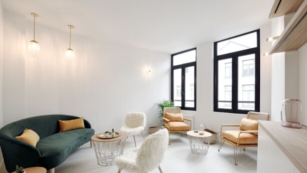 A modern living room with a green sofa, white chairs, and a wooden coffee table. There are large windows and a plant in the room. - Urban Walls (Brussels)
