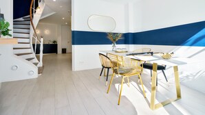 A modern interior with a staircase, a dining area with a white table and yellow chairs, and a blue accent wall. - Urban Walls (Brussels)