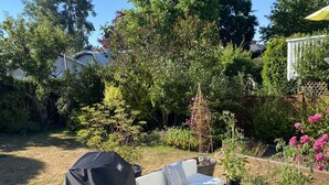 A patio with outdoor furniture, including a sofa and a table, surrounded by potted plants and a wooden deck.