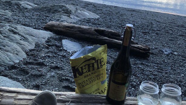 A log with a bottle and a bag of chips on a rocky shore.