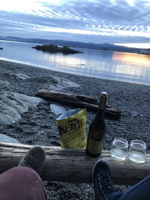 A log with a bottle and a bag of chips on a rocky shore.