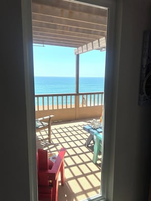 Vista a través de una puerta que da a un balcón con baranda de madera, una mesa y una silla.
