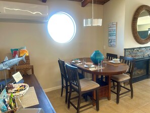 Uma sala de jantar com uma mesa redonda, cadeiras, uma escultura decorativa de peixe, uma cesta trançada e um espelho fixado na parede.