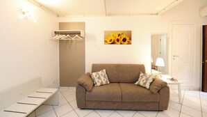 A modern living room with a sofa, a small table with a lamp, a coat rack, and a painting of sunflowers. - Cozy home in a historic building in the heart of Amalfi, steps from the sea (AMALFI)