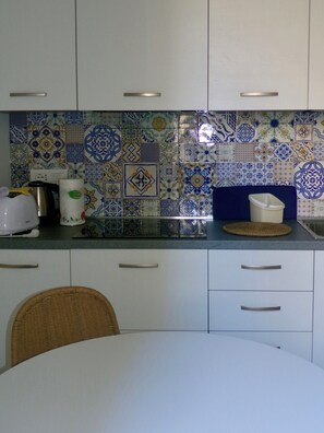 A kitchen with patterned tiles, a white countertop, a kettle, a coffee maker, and a wicker chair. - Cozy home in a historic building in the heart of Amalfi, steps from the sea (AMALFI)