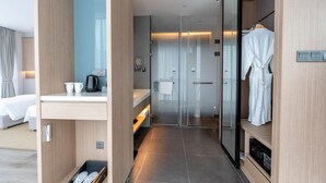A modern hotel room with a bed, a bedside table with a coffee maker, a glass shower enclosure, and a robe hanging on a rack. - Novotel Shanghai Qingpu Excellence (Shanghai)