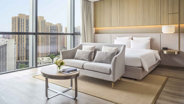 A modern hotel room with a large window, a sofa, a bed, and a small table with a vase of flowers. - Novotel Shanghai Qingpu Excellence (Shanghai)