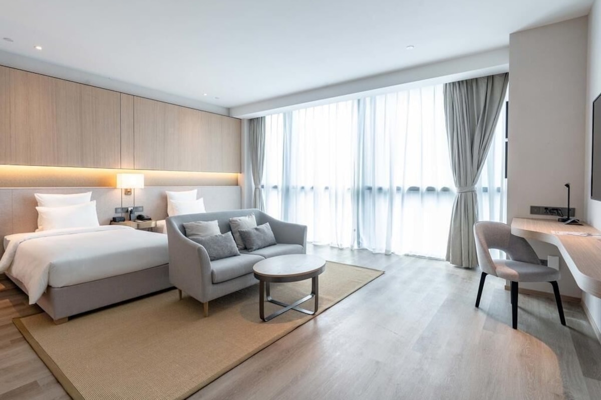 A modern hotel room with a bed, sofa, round coffee table, and a desk.