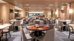 A spacious hotel dining area with multiple round tables, chairs, and a central kitchen area visible through the glass wall. - Novotel Shanghai Qingpu Excellence (Shanghai)
