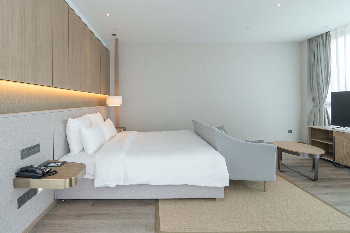 A modern hotel room with a bed, bedside table, lamp, and a TV.