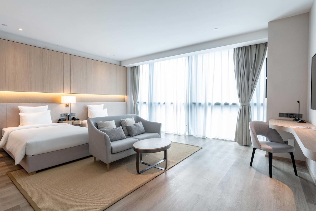 Ett modernt hotellrum med en säng, soffa, ett litet runt bord och ett skrivbord med stol.