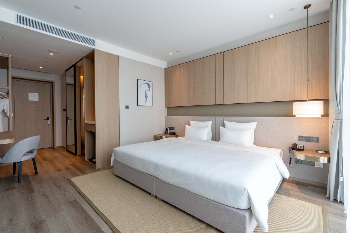 A modern hotel room with a large bed, a desk, and a chair.
