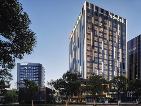 A modern hotel with a prominent 'Novotel' sign, surrounded by other high-rise buildings and trees.