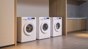 Three front-loading washing machines in a modern laundry room with tiled flooring and wooden cabinetry. - Novotel Shanghai Qingpu Excellence (Shanghai)