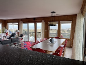 A cozy room with a dining table, chairs, and a view of the ocean through large windows.