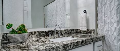A bathroom with a granite countertop, a white sink, a mirror, a shower curtain, and a potted plant.
