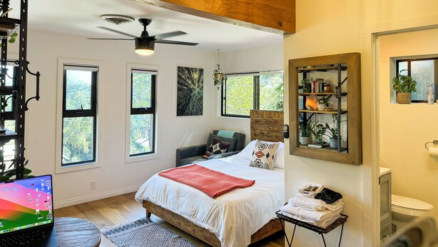A bedroom with a bed, a ceiling fan, a window, a bookshelf, and a bathroom. - Modern-Rustic Canyon Studio with Kitchen Close to Hiking in Los Angeles. (Sierra Madre)