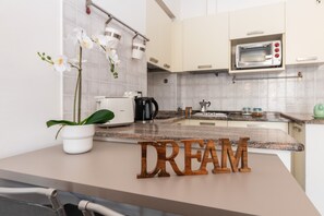 A modern kitchen with white cabinets, a microwave, a coffee maker, and a plant on the counter.