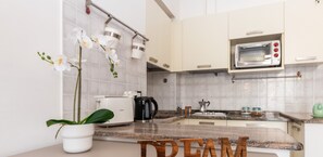 Cocina moderna con armarios blancos, microondas integrado y encimera con cafetera y planta de orquídea.