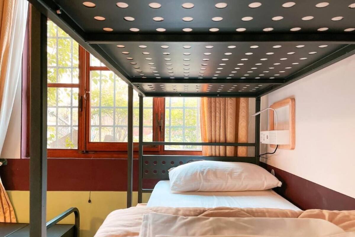 Dormitorio con literas, ventana, cortinas y lámpara fijada a la pared.