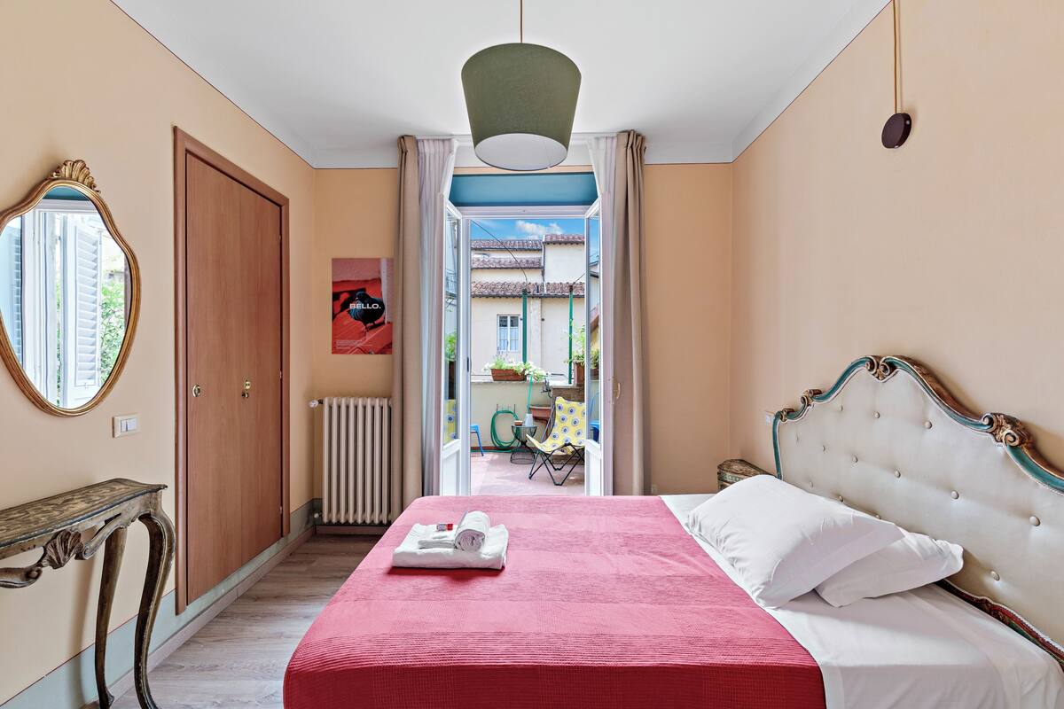 Un dormitorio con cama, espejo, radiador y puerta abierta que da a un espacio exterior.