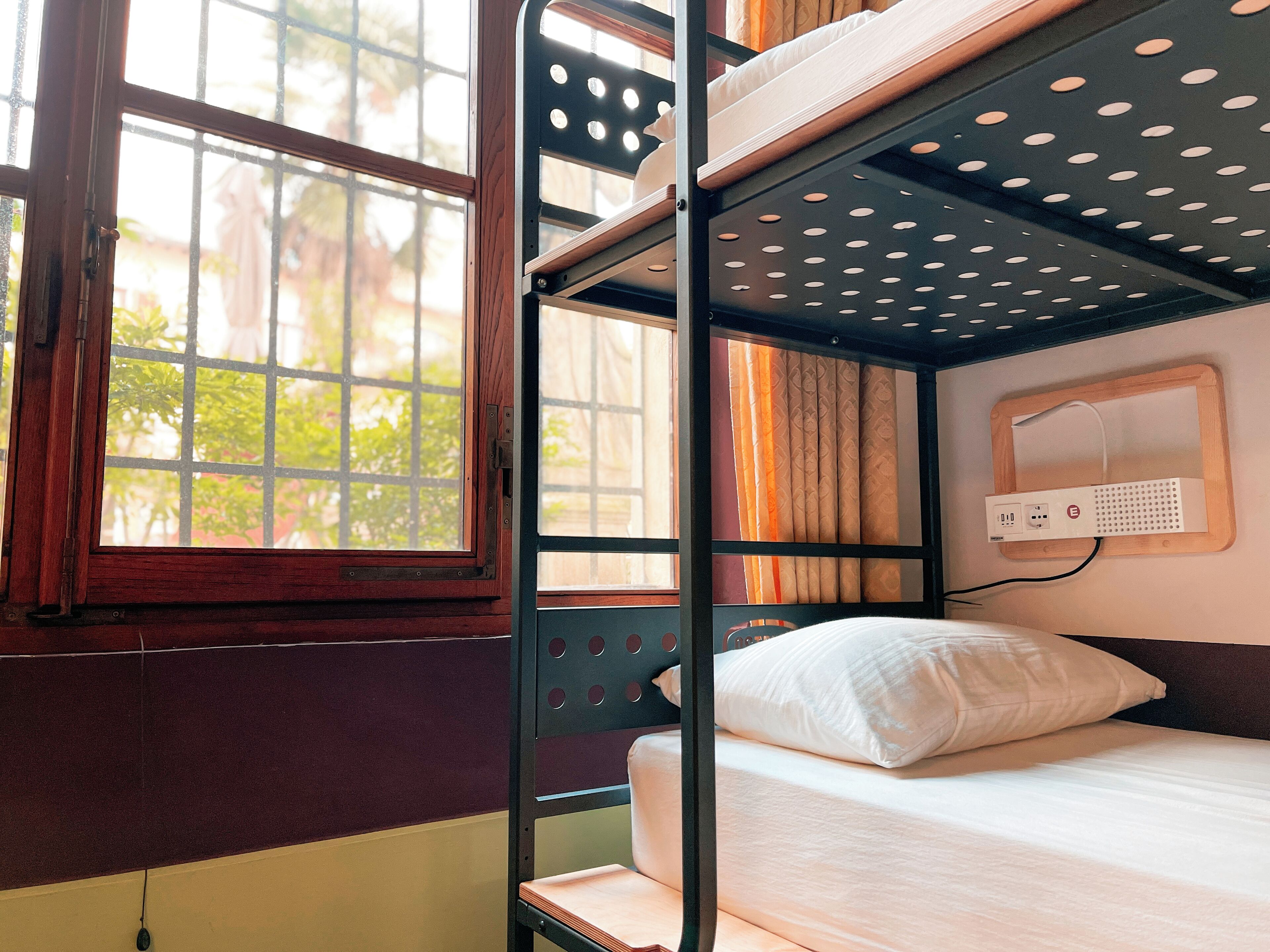 A bunk bed with a power outlet and a window with a view of greenery.