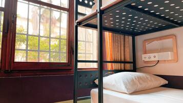 A bunk bed with a power outlet and a window with a view of greenery.