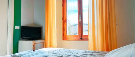A bedroom with a bed, a television on a small table, and a window with curtains.