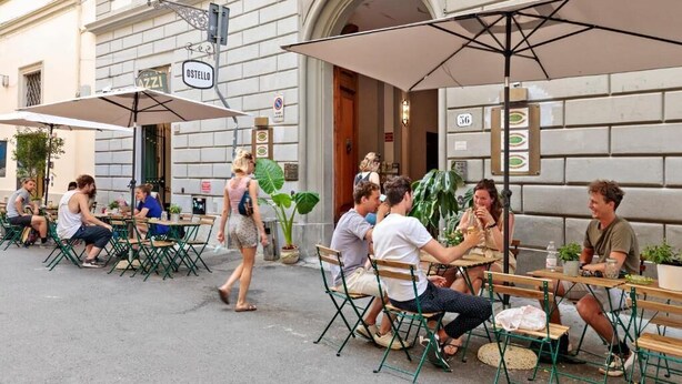 Outdoor seating with umbrellas, a street view, and a building with a sign reading "OSTELLO". - Ostello Bello Firenze (Florence)
