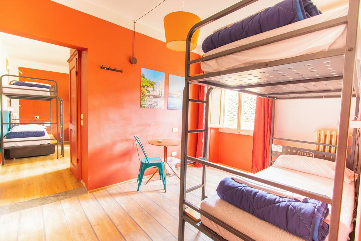 Habitación con literas, paredes anaranjadas, una mesita pequeña y una silla.