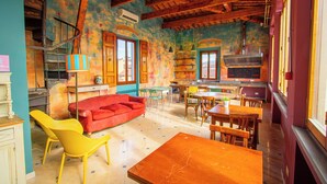A spacious room with a wooden ceiling, a red sofa, yellow chairs, a wooden table, and a kitchen area with a stove and cabinets. - Ostello Bello Firenze (Florence)