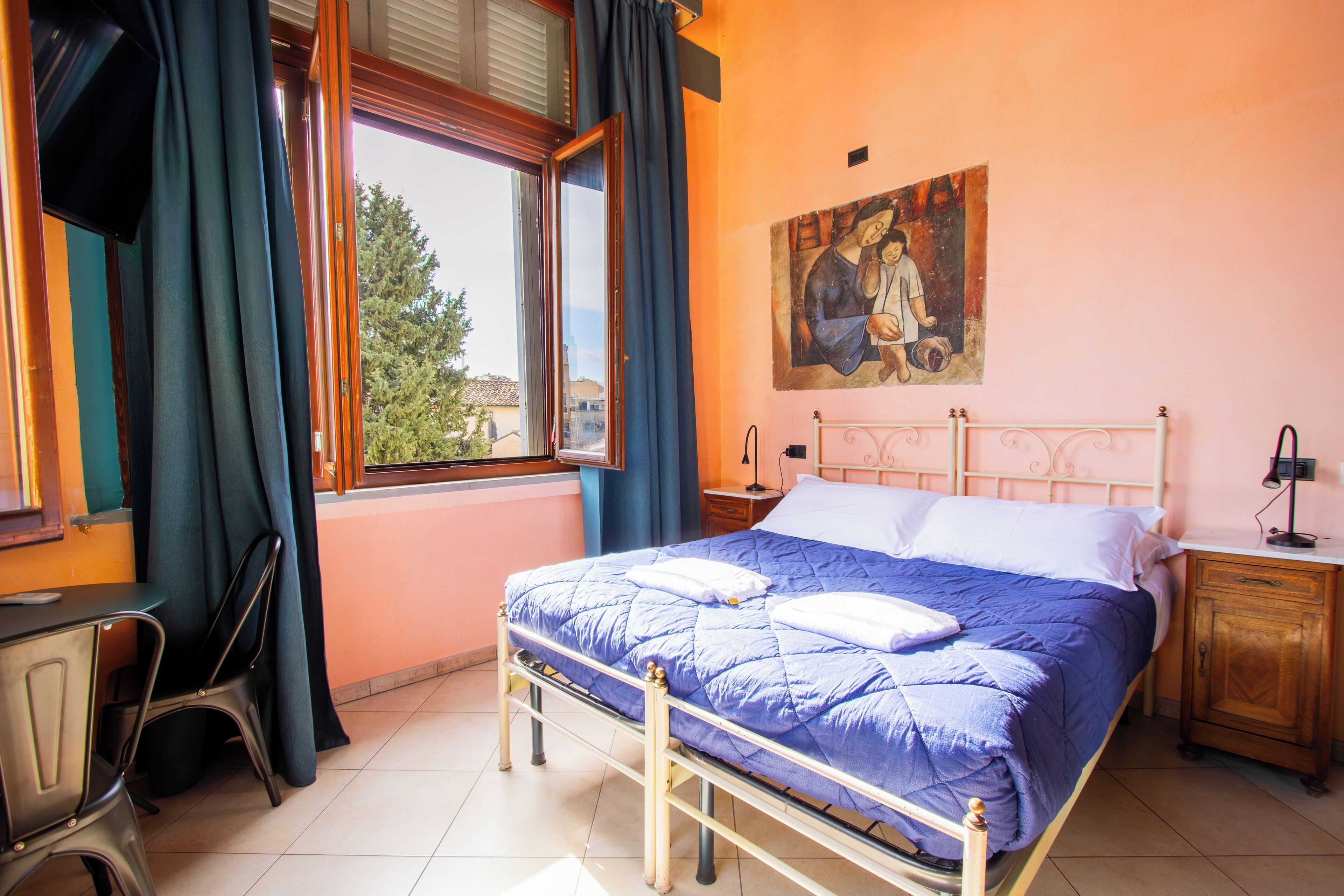 Une chambre à coucher comprenant un lit, une table de chevet, une chaise, une fenêtre avec des rideaux et un tableau accroché au mur.