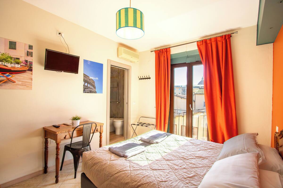 Una habitación de hotel con cama, escritorio con silla, televisión y ventana con cortinas.