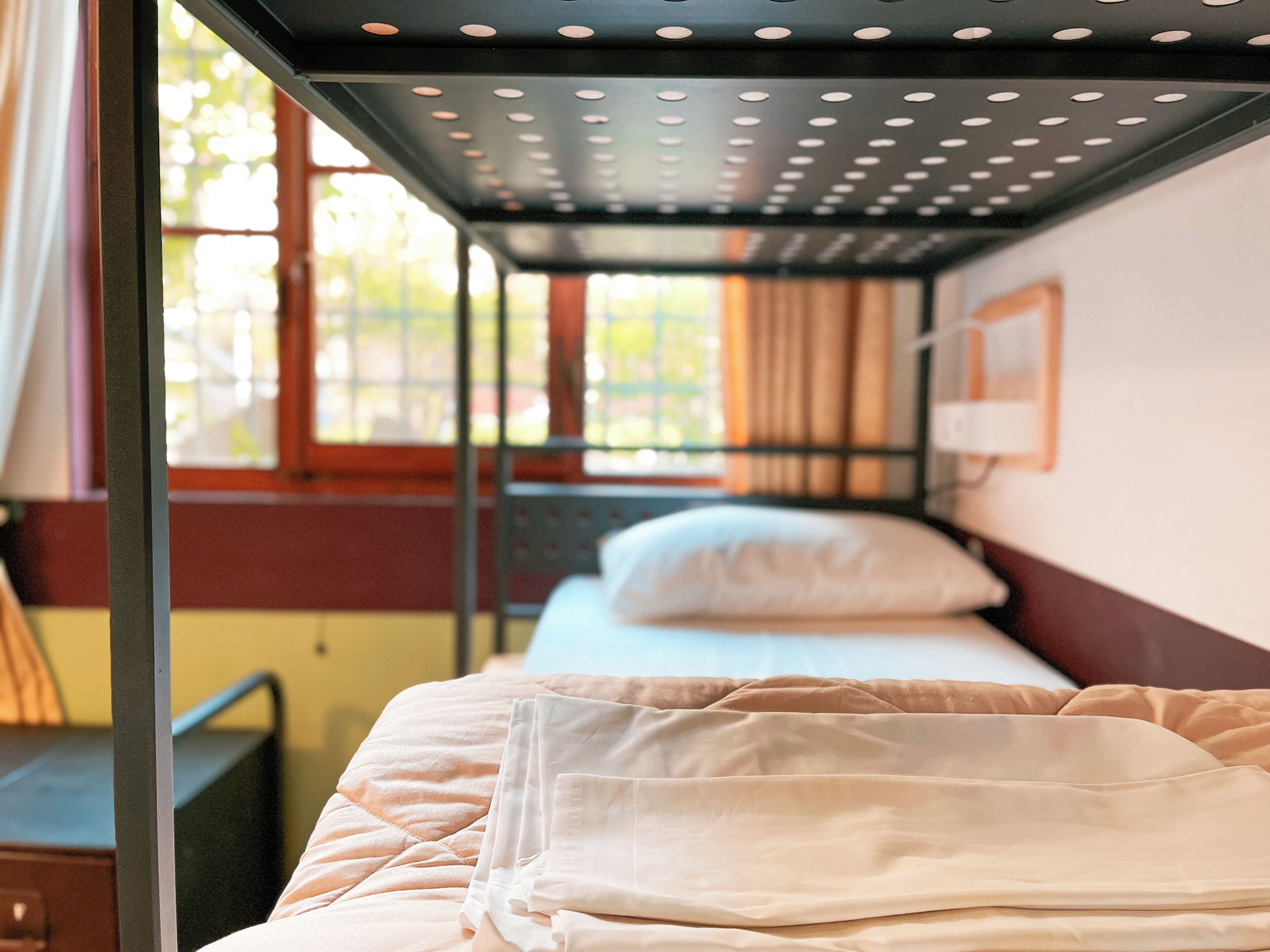 A bunk bed with a quilted mattress and a headboard, a window with curtains, and a wall-mounted picture frame.